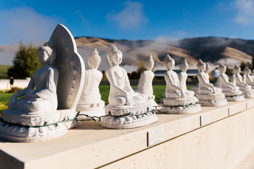 A collection of white buddha statues lining the top of a wall with mountains in the background.