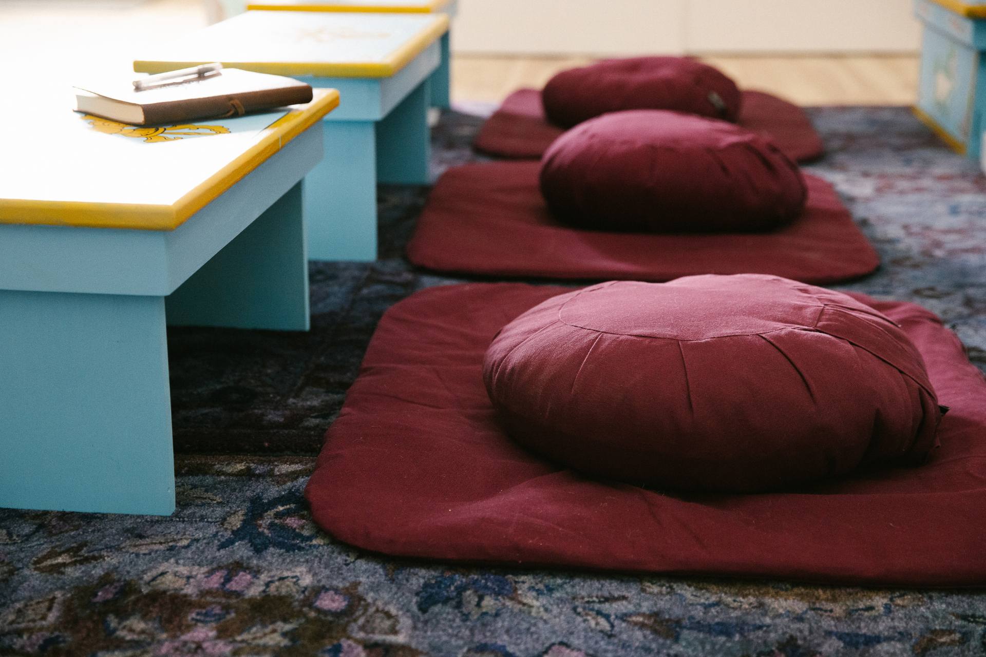 cushion Close-up of burgundy meditation cushions in a row behind a row of short, light blue desks.