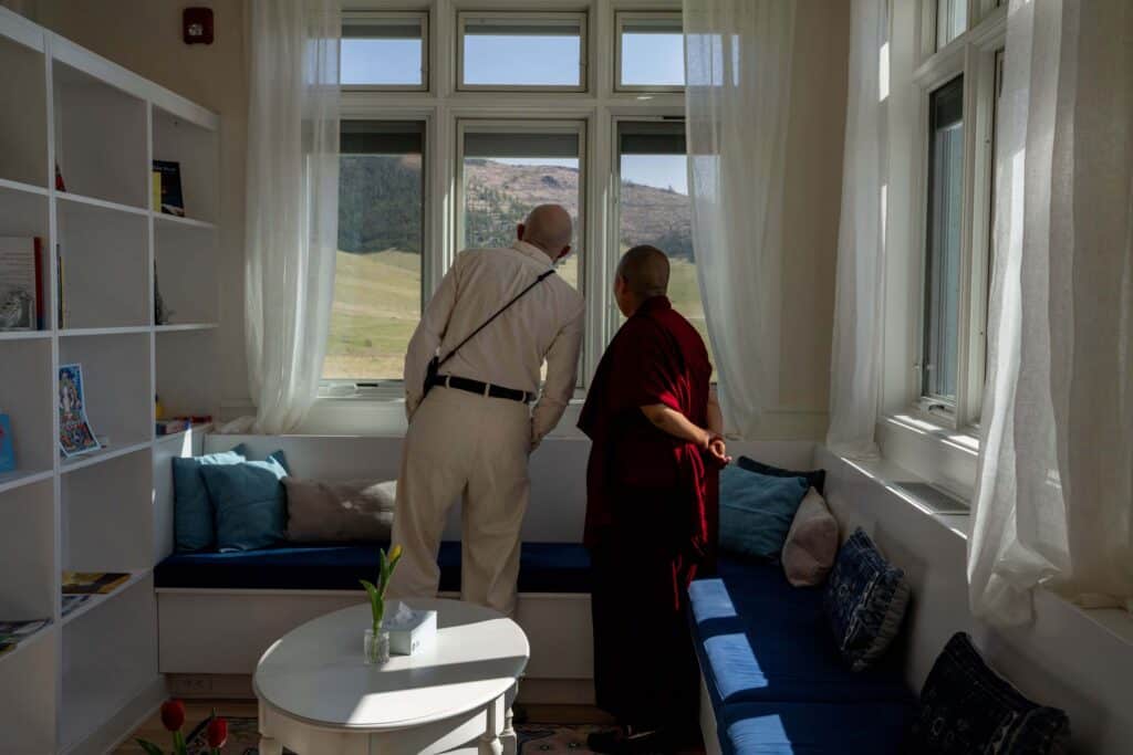 Justin Kirkwood and Dorlop Choenyi Sangmo look out a large window together at the Montana landscape from a cozy library area.