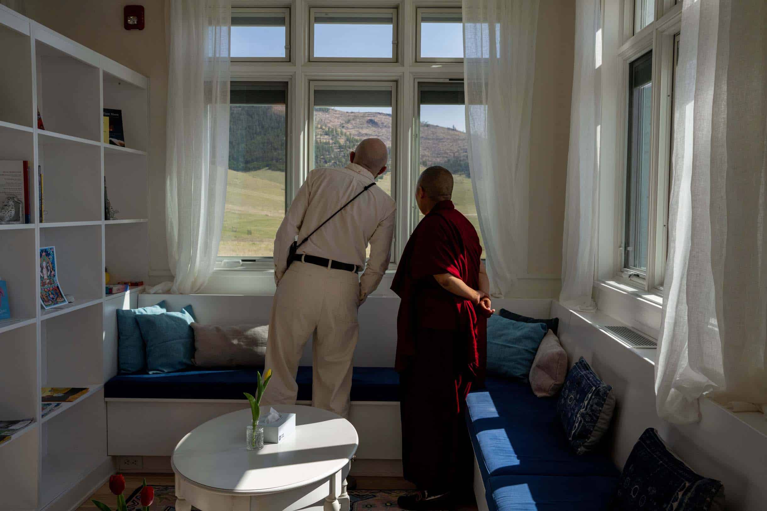 Justin Kirkwood and Dorlop Choenyi Sangmo look out a large window together at the Montana landscape from a cozy library area.