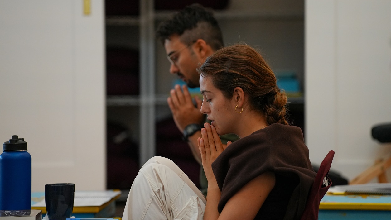 Man and woman with hands in prayer position during a meditation retreat.