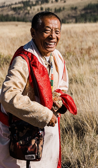 Gochen Tulku Sangak Rinpoche in traditional Tibetan clothing walking joyfully through a golden field, throwing rice.