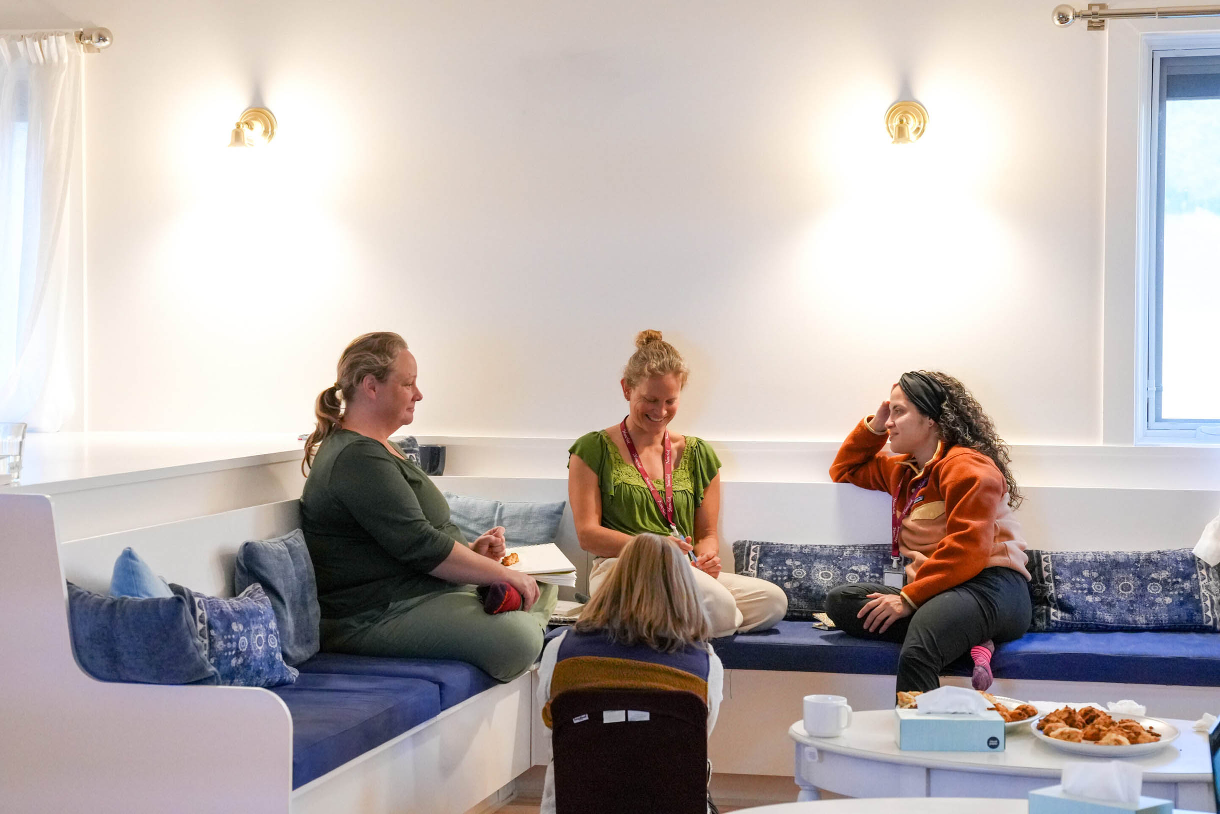 A group of women sitting in a circle on a built-in bench, smiling and sharing during a mindfulness workshop.
