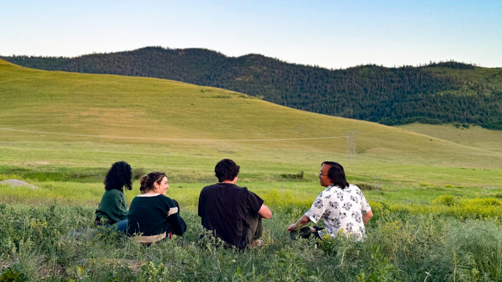 Students sitting in grass overlooking mountains.