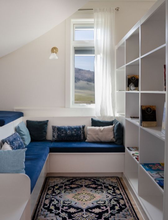 Cozy and peaceful accommodation with a built-in seating nook, soft cushions, natural light from a window, and minimalist shelving creating a calm retreat space