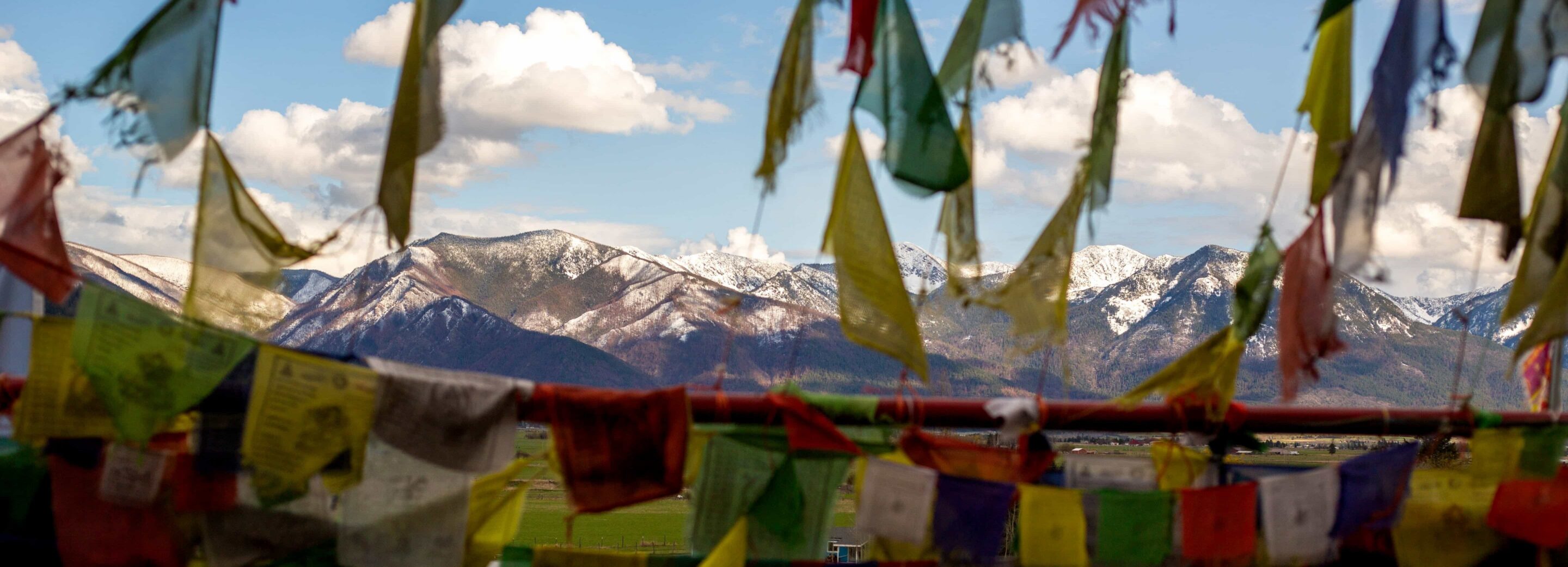 Colorful Tibetan prayer flags with snow-capped mountains in the background under a blue sky.